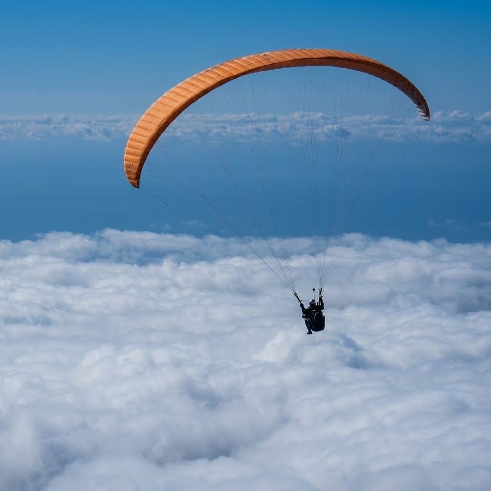 Parapente volando sobre un mar de nubes