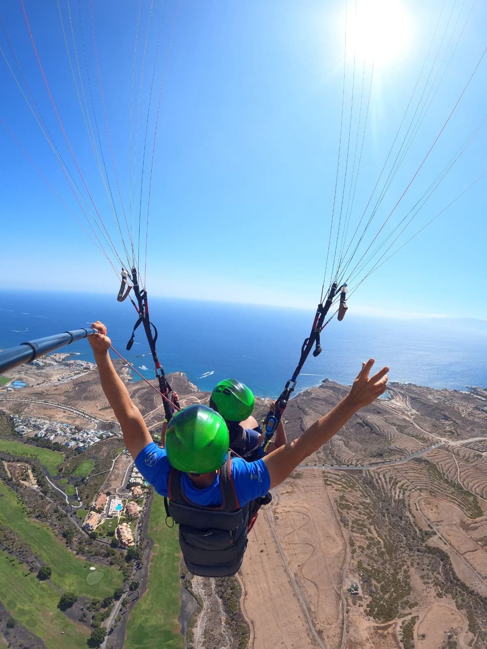 Pasajeros con cascos verdes celebrando durante el vuelo en parapente sobre la costa de Tenerife