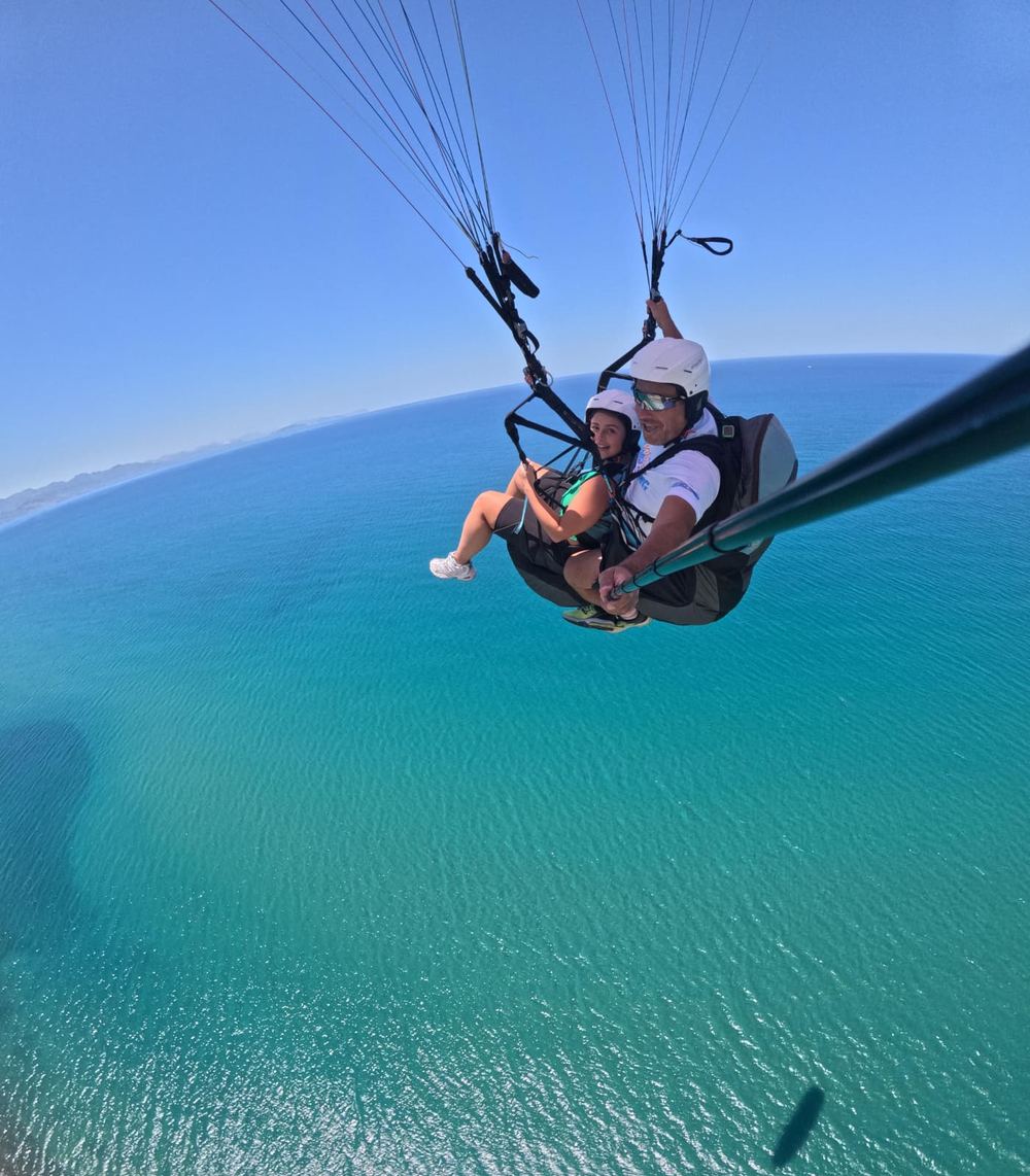 Pareja sonriendo en vuelo biplaza de parapente sobre el mar turquesa de Tenerife